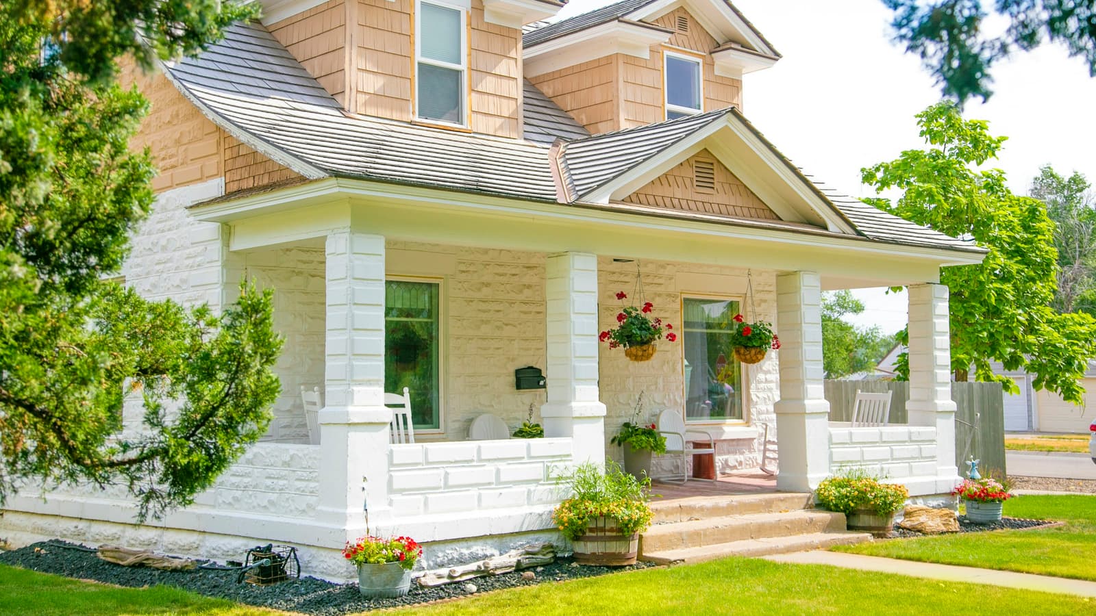 Cream-colored house with a covered front porch, landscaped flower beds and a neat green lawn