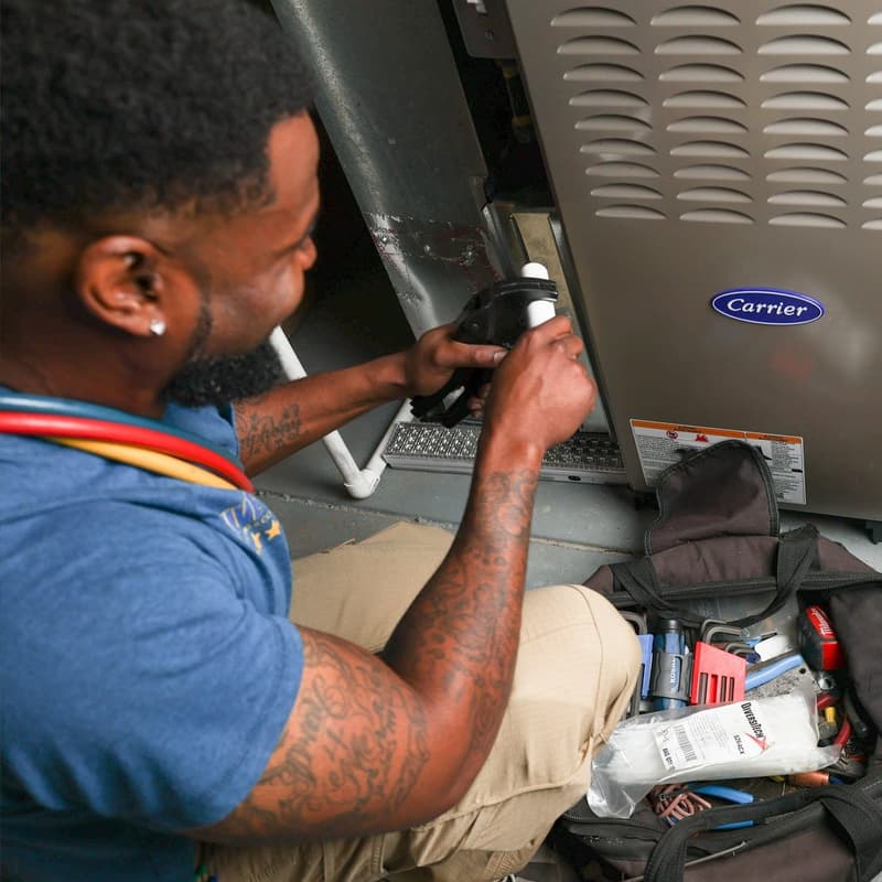 Technician working on a Carrier furnace with tool bag