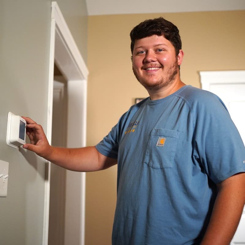 Smiling technician adjusting a wall thermostat indoors