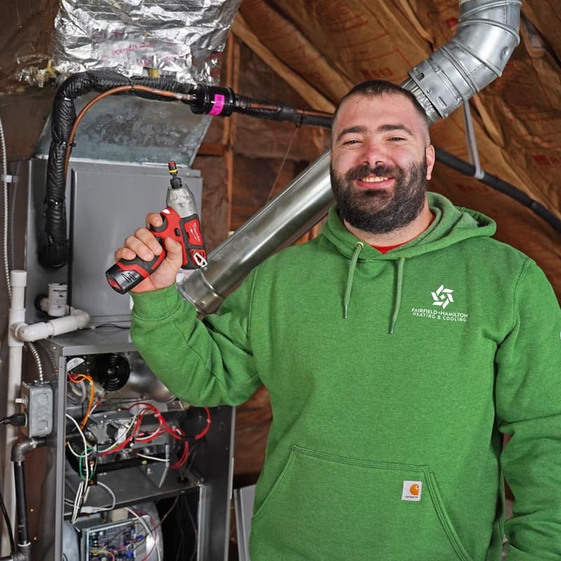 Technician holding a drill beside furnace and ductwork in attic